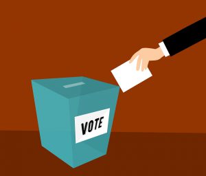 box with the word vote on it and a hand putting paper towards the box
