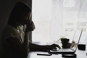 woman sitting at a desk with coffee in her hand and looking at a laptop