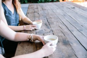 two people sitting down at a wooden table with coffee in their hands