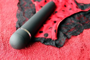 a black vibrator laying on top of red underwear with black polka dots