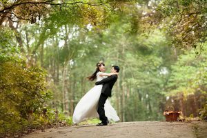 asian woman and man in wedding outfits hugging in the forest.