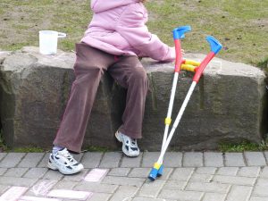 child sitting on a stone row with crutches leaning on the stone row next to child.