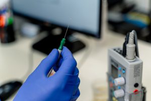hand with a blue glove holding a needle