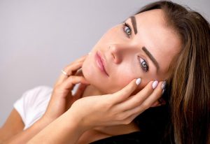 young looking caucasian woman touching her face.
