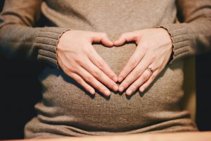 womans hands cresting a heart over her pregnant stomach