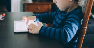 young caucasian boy sitting at a table looking at a tablet