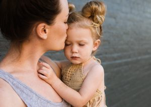 caucasian woman holding a young girl and kissing her head.