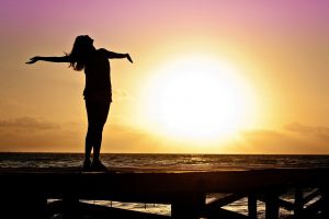 silhouette of a woman with her hands out and head facing up with a sunset in the background