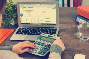 laptop screen with bank account on it and hands holding a calculator over the keyboard