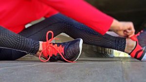 legs of a woman in red workout pants tying her shoe lace of her sneaker