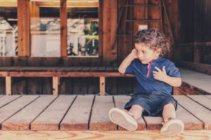 toddler sitting down touching his ear