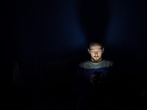 young man sitting in the dark staring at his phone