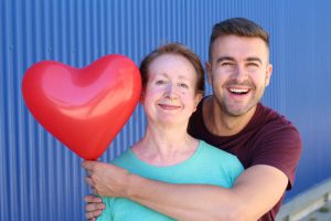 young man hugging an older woman while holding a red heart balloon