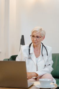 caucasian woman with a white coat on and stethoscope over her neck looking at a laptop screen