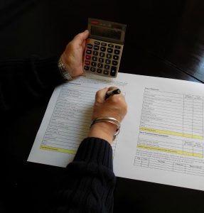 womans hands, one holding a calculator and the other writing on a large piece of paper