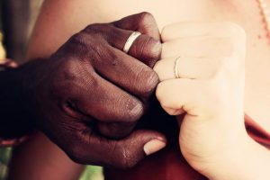 african american hand holding a caucasian hand with wedding rings on the ring fingers