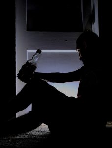 black and white picture of a person sitting on the floor with a bottle of alcohol in their hand