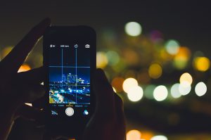 hands holding a cell phone taking a picture of the night skyline