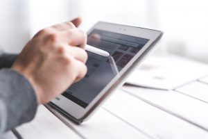 a hand holding a white stylus onto a tablet screen