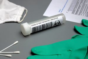 covid test tube with a swab next to it and green gloves.