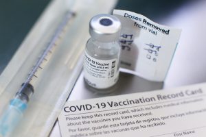 covid vaccine vial with a needle next to it and vaccine card