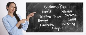 woman in a blue button up with a business plan written on a chalkboard