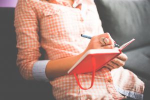 woman's torso sitting down writing in a red journal