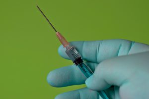 hand with a blue glove on it holding a needle.