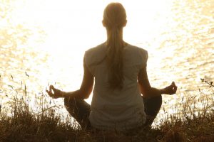 back of a woman sitting in front of water meditating