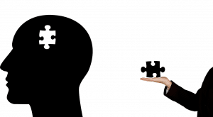 silhouette of a head with a white puzzle piece missing and a person's hand holding the puzzle piece