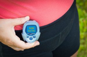 woman holding a pedometer on her waist that says 10,000 steps today on it 