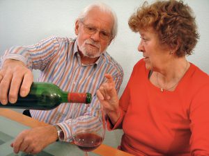 woman sitting next to man pouring her a glass of wine with her fingers pinching a size