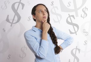 woman in a blue button up shirt with her hand on her chin and question marks around her