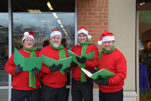 4 people dressed in red sweatshirts with santa hats holding green books