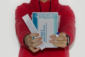 person with red shirt holding up covid testing kit