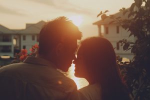 a man and woman looking at each other closely with a sunset in the background