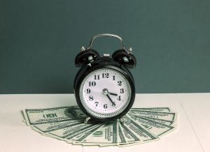 black alarm clock placed on top of hundred dollar bills