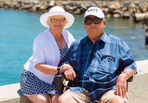 an older man and woman couple smiling with body of water behind them