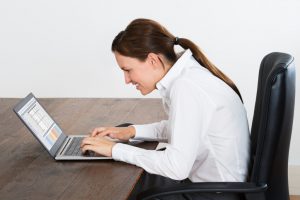caucasian woman with work attire sitting at a desk slouching while looking at her laptop