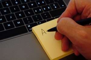 hand holding a pen writing on a post it note