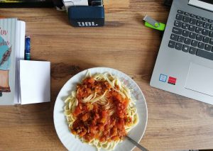 plate of spaghetti on a desk next to a laptop