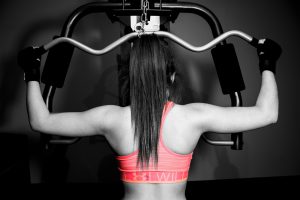 black and white picture of a woman sitting at the lateral machine doing a pull down with a pink sports bra on