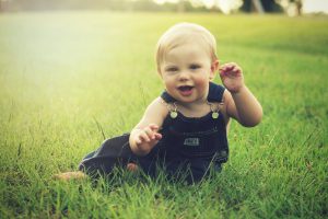 caucasian baby in overalls sitting on grass 