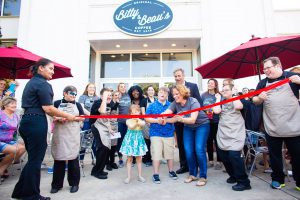red ribbon about to be cut with the bitty and beau shop behind it