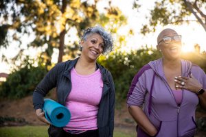 two older african american women in workout attire with one holding a yoga mat