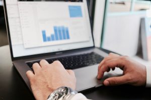person's hands on a laptop keyboard with a graph on a screen