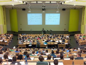 university classroom with people in it in and a professor in front teaching