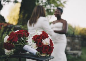 two women in white getting married in the background behind roses