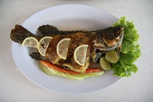 whole cooked fish on a plate with lemons on it and olives next to it
