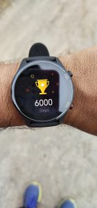 hand with a fitness tracker on it and a trophy on the screen with 6000 steps